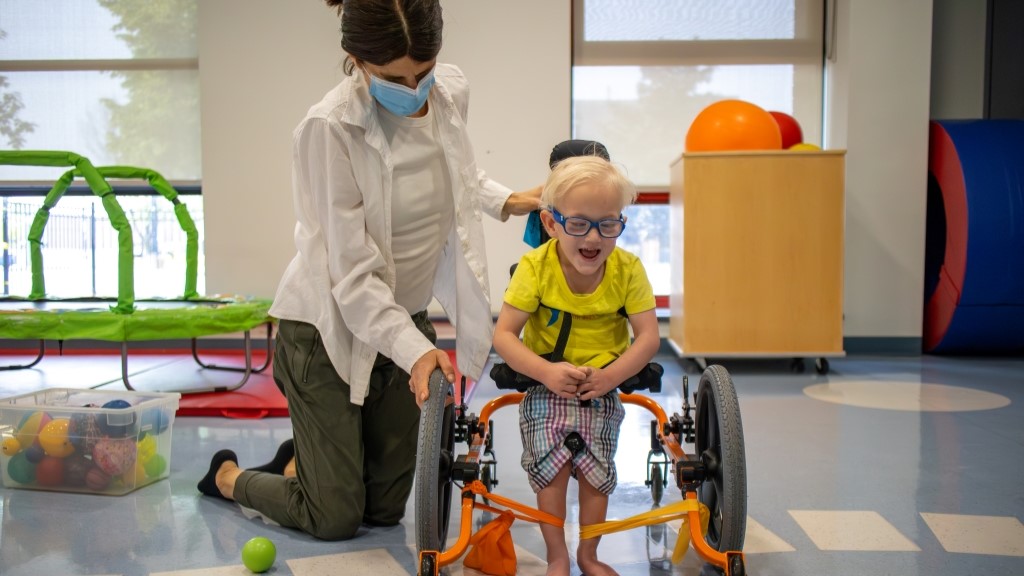 Women helping young boy in a walker in a treatment room