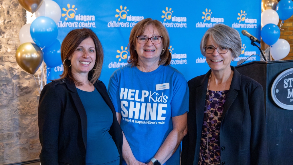 Three women in front of blue backdrop with balloons