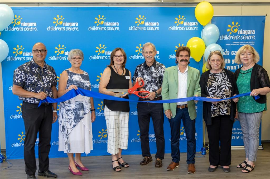 Group of people cutting ribbon in front of blue backdrop
