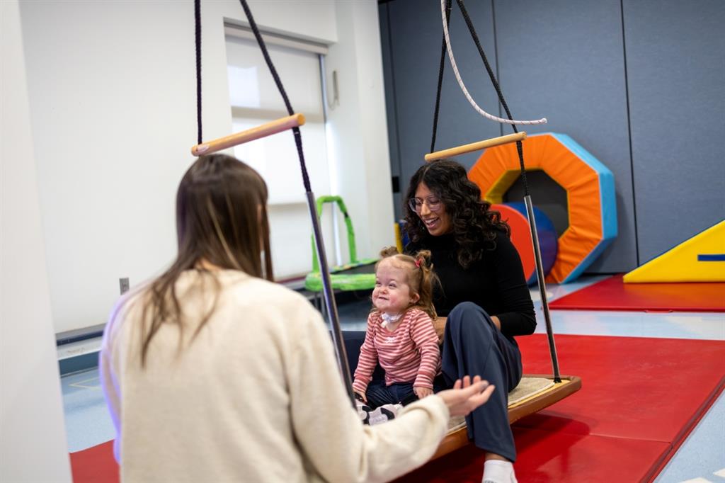 Two women and a child on swing in therapy room