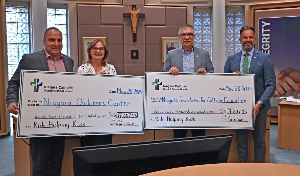 Four people holding large cheque in meeting room