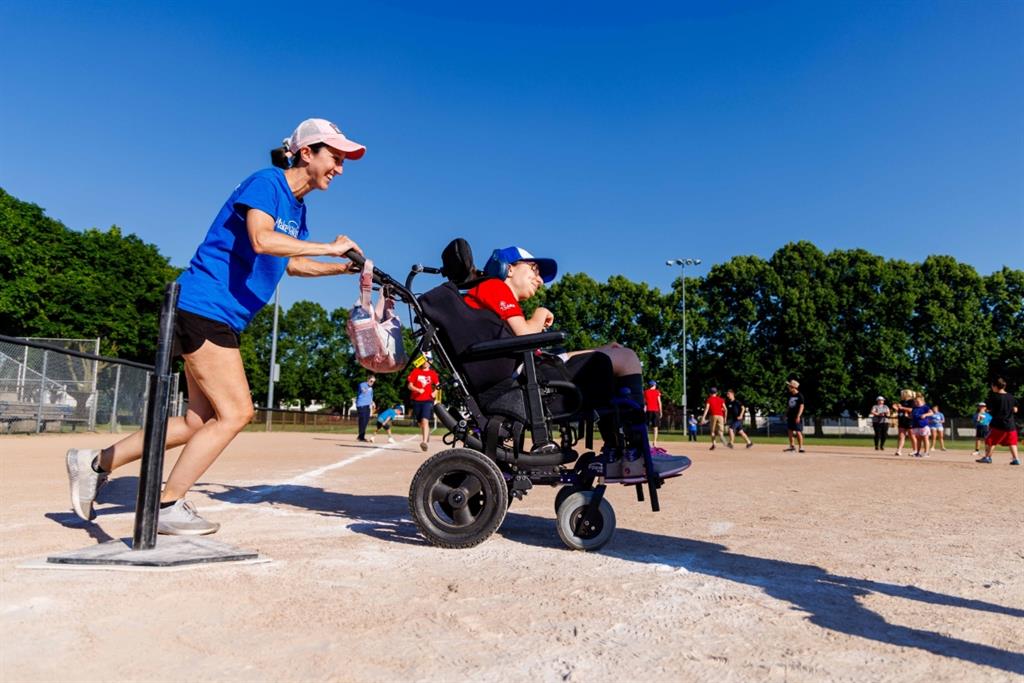 Women pushing girl in wheelchair on baseball daimond
