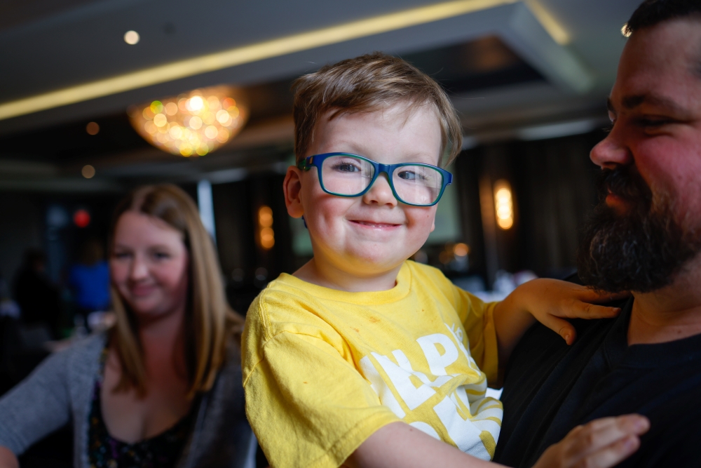 Boy wearing yellow t-shirt and blue glasses smiling
