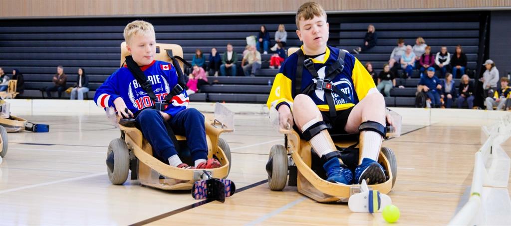 Two boys in VOLT hockey chairs chase ball on gym floor