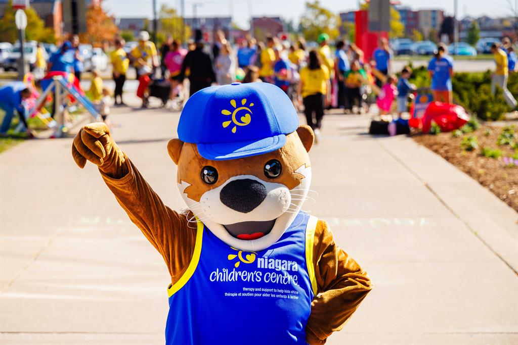 An otter mascot poses with one arm raised in front of a crowd