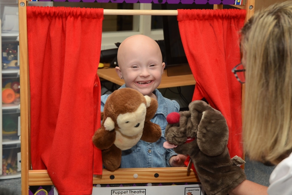 Young girl hosting a pupppet show with red curtains