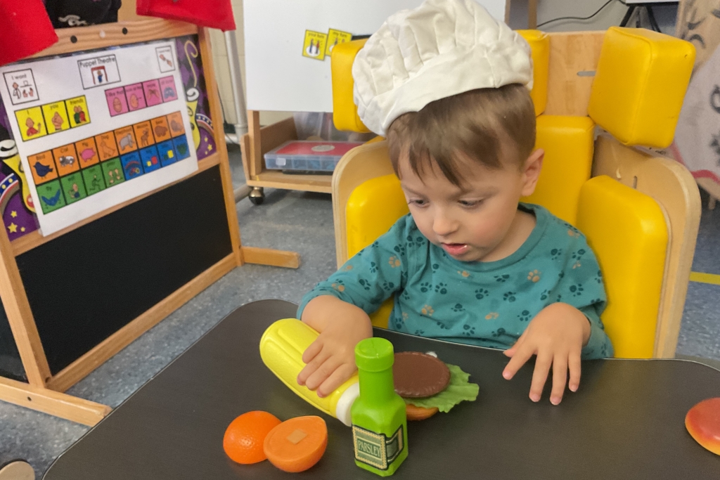 Young boy wearing chef hat, holding mustard bottle