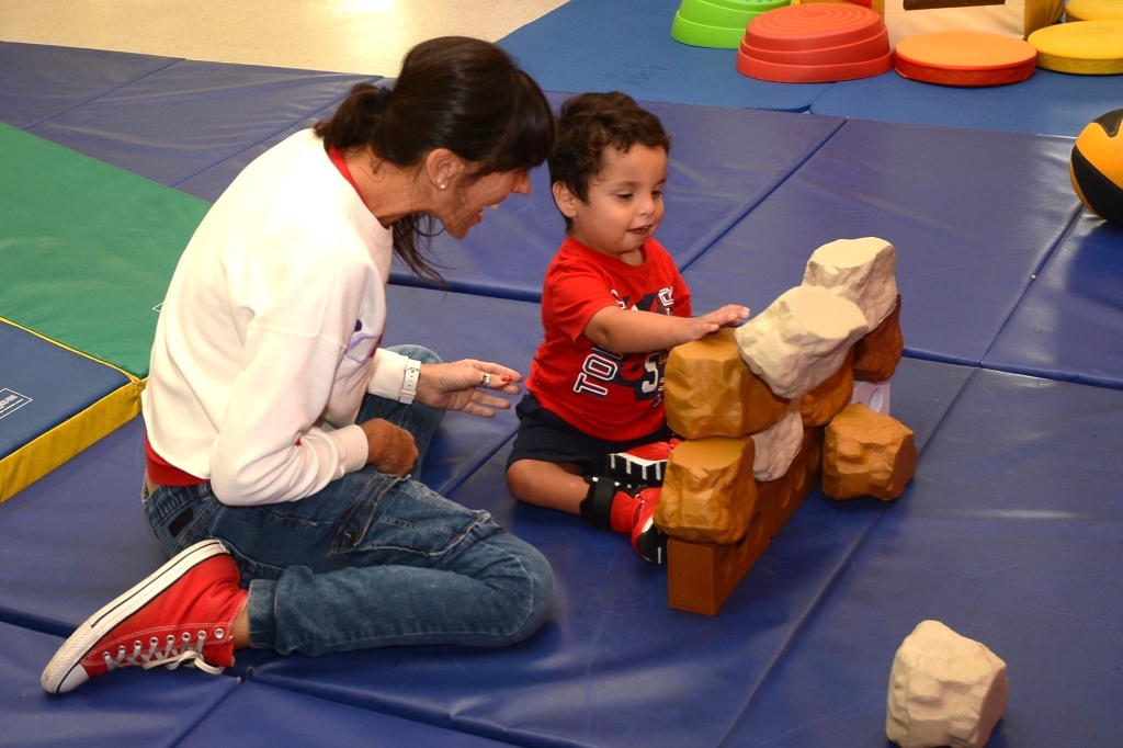 Female teaching watching young male student push blocks